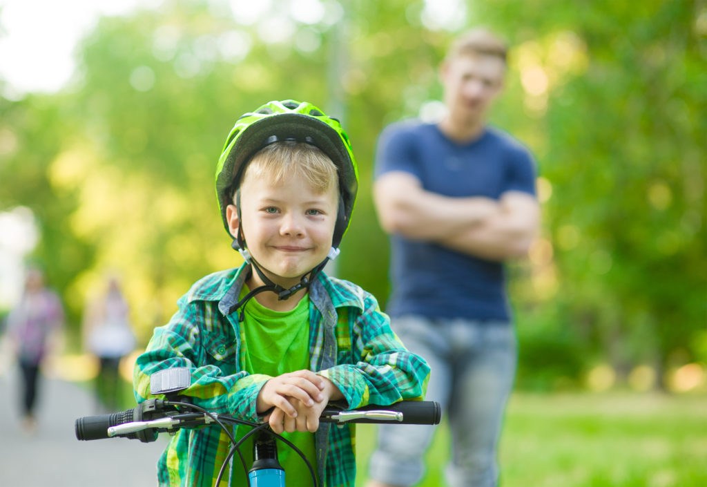 Boy on a bike with a happy father behind him
